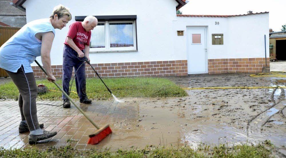 Veronika und Steffen Schwind reinigen den Gehweg vor ihrem Haus, der voller Schlamm ist.