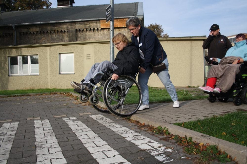 Wo der Fußweg auf dem Einkaufsmarkt-Parkplatz weitergeht, ist gekennzeichnet. Doch Rollstuhlfahrer Klaus Stegmann kann den Bordstein nicht passieren; Astrid Staudenraus hilft ihm.