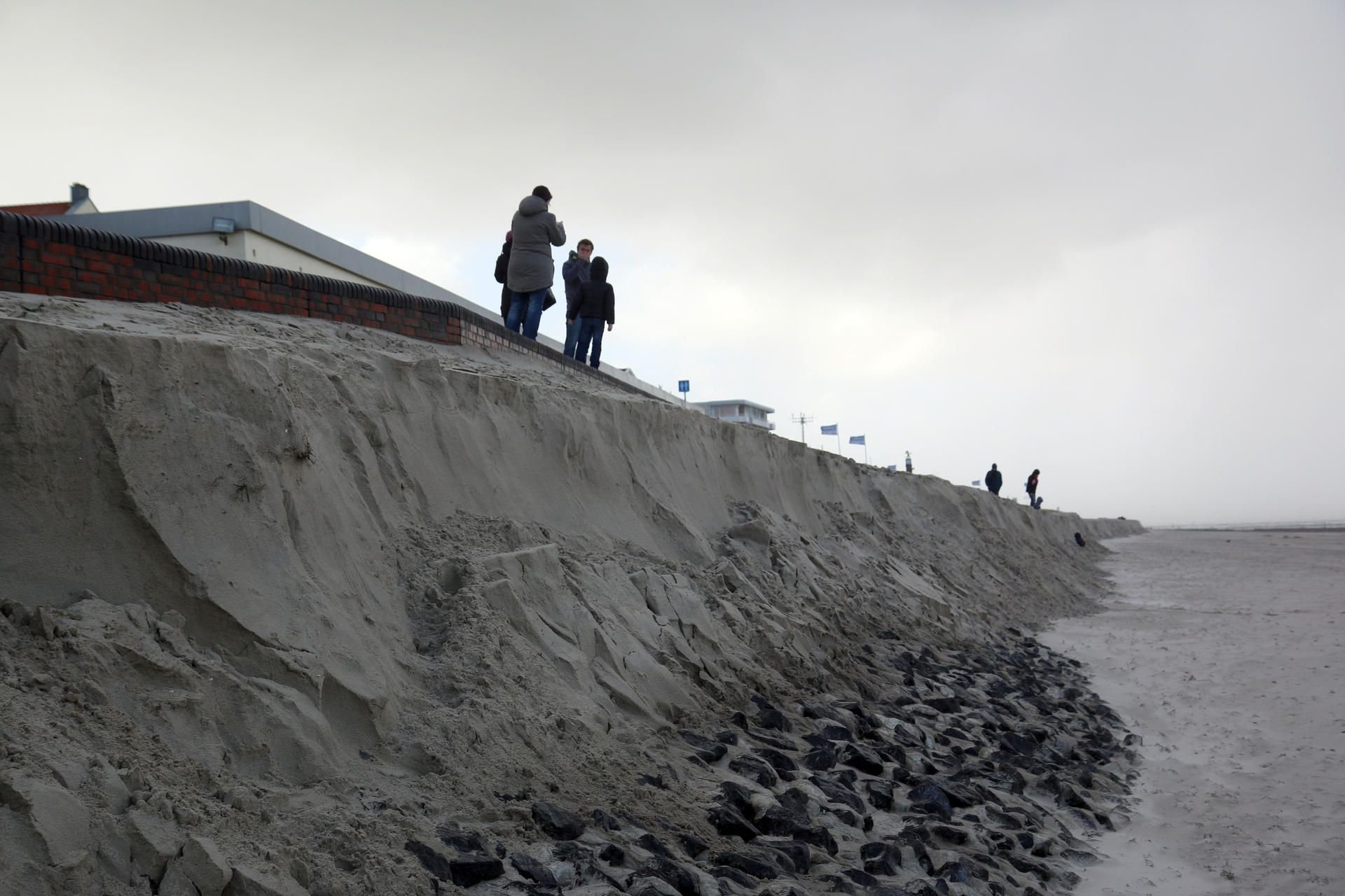 Passanten stehen auf Wangerooge an der Abbruchkante im Mittelfeld des Bade- und Burgenstrandes.