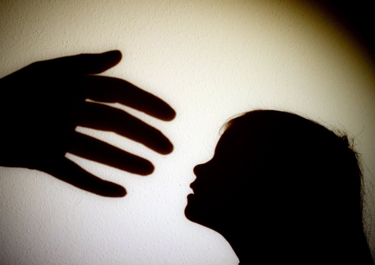 Schatten einer Hand einer erwachsenen Person und der Kopf eines Kindes an einer Wand eines Zimmers,
