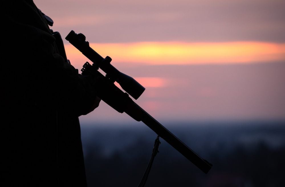 Ein Jäger hält sein Gewehr in der Dämmerung.