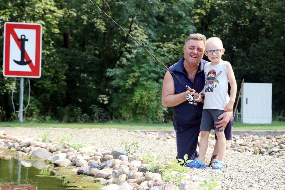Inhaber Holger Schneider steht mit seinem Enkel, dem fünfjährigen Finn, an einem Teich im „Forellenparadies“.