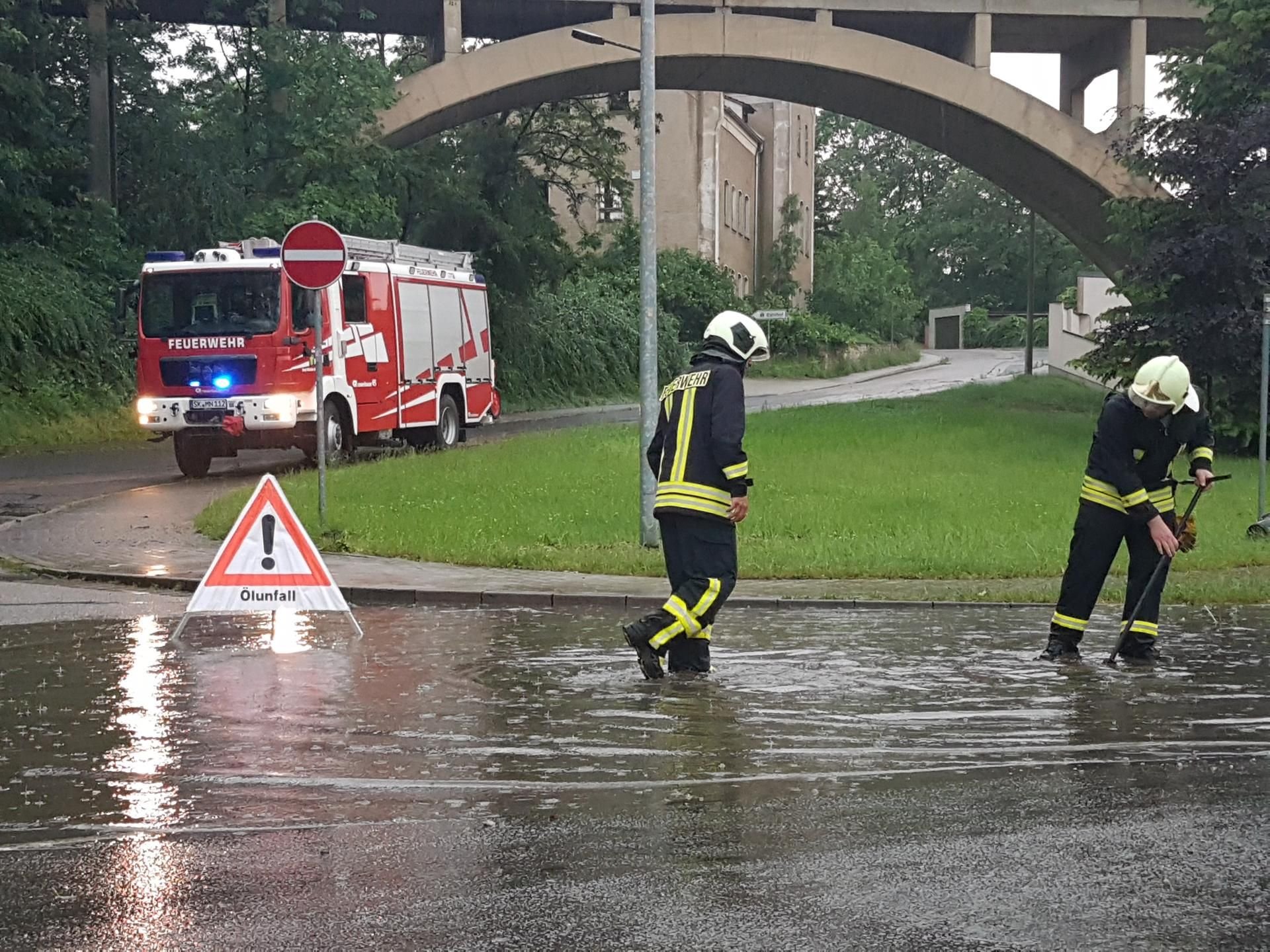 Überschwemmung am Kreisel in Mücheln. Feuerwehrleute suchen nach einem Gully, um das Wasser abfließen zu lassen.