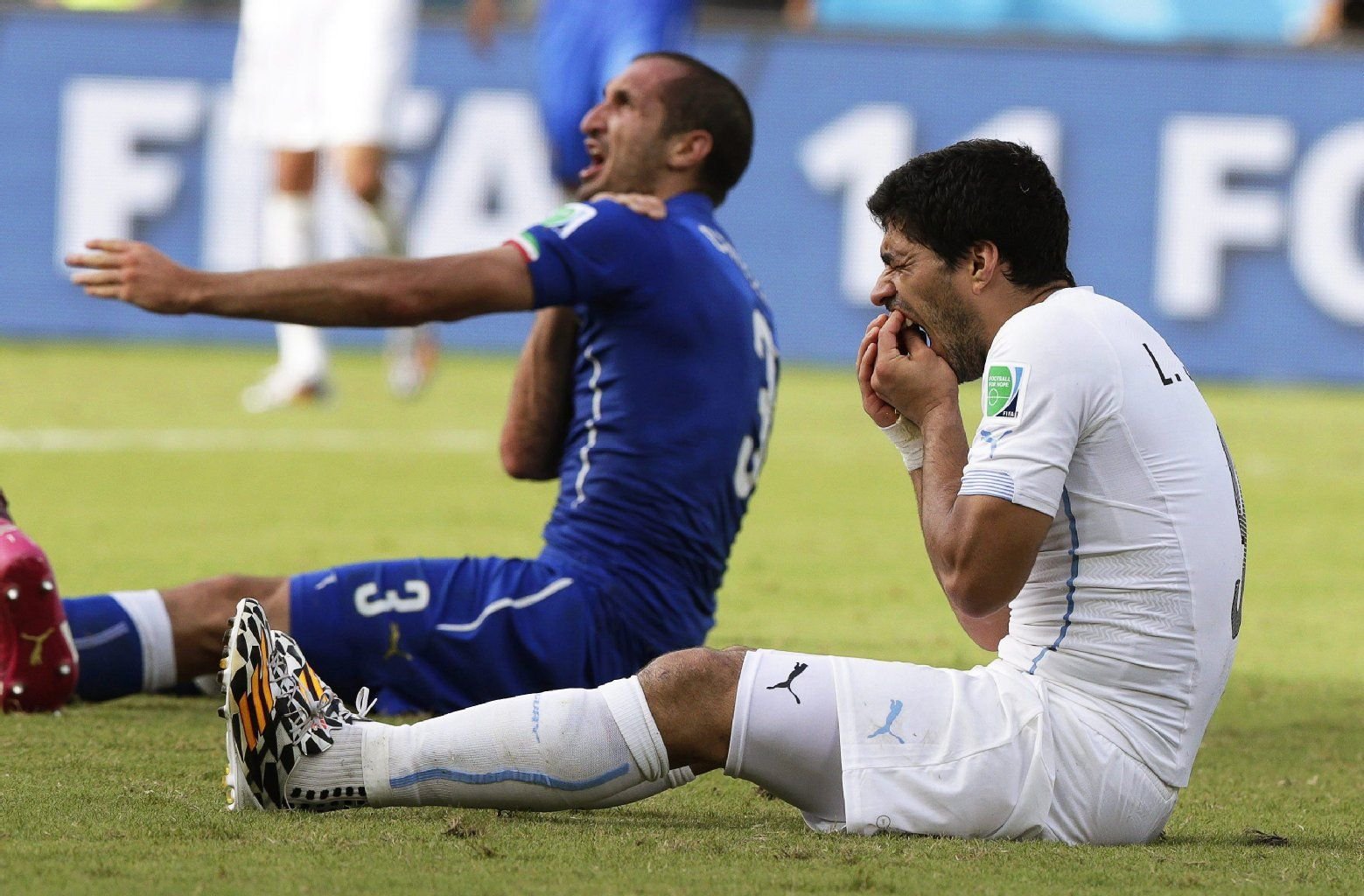 Italien-Profi Giorgio Chiellini beschwert sich, während sich Luis Suárez nach seiner Beiß-Attacke die Zähne hält.