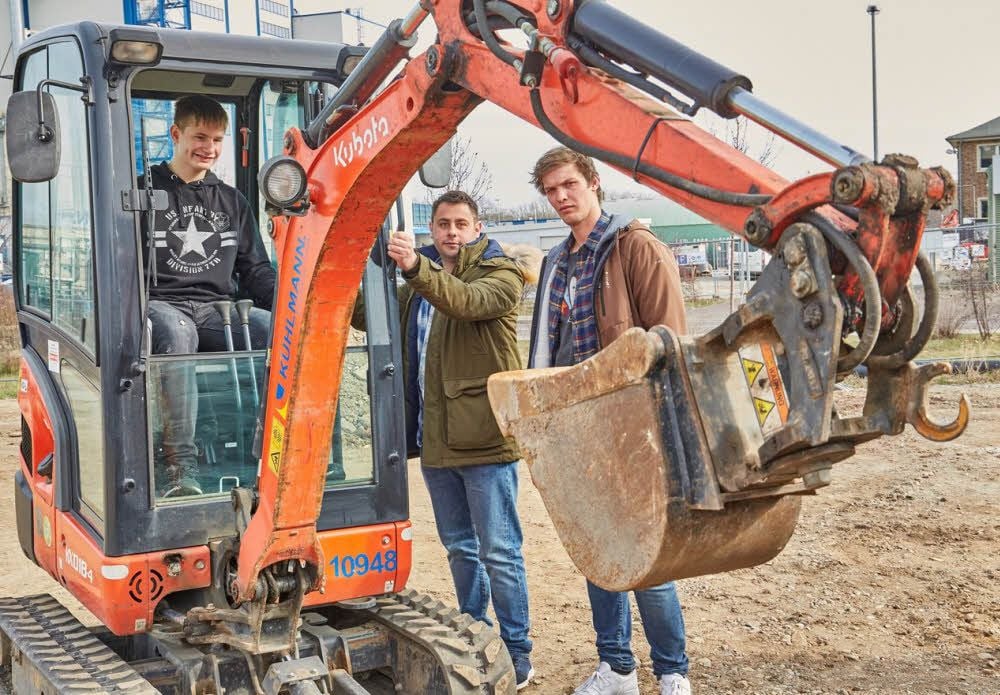 Sebastian Hamann (von re.) und Fabian Konrad zeigen Justin Wendtland, wie man einen Bagger steuert.