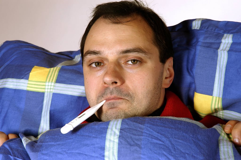 Ein kranker Mann liegt mit Fieberthermometer im Bett.