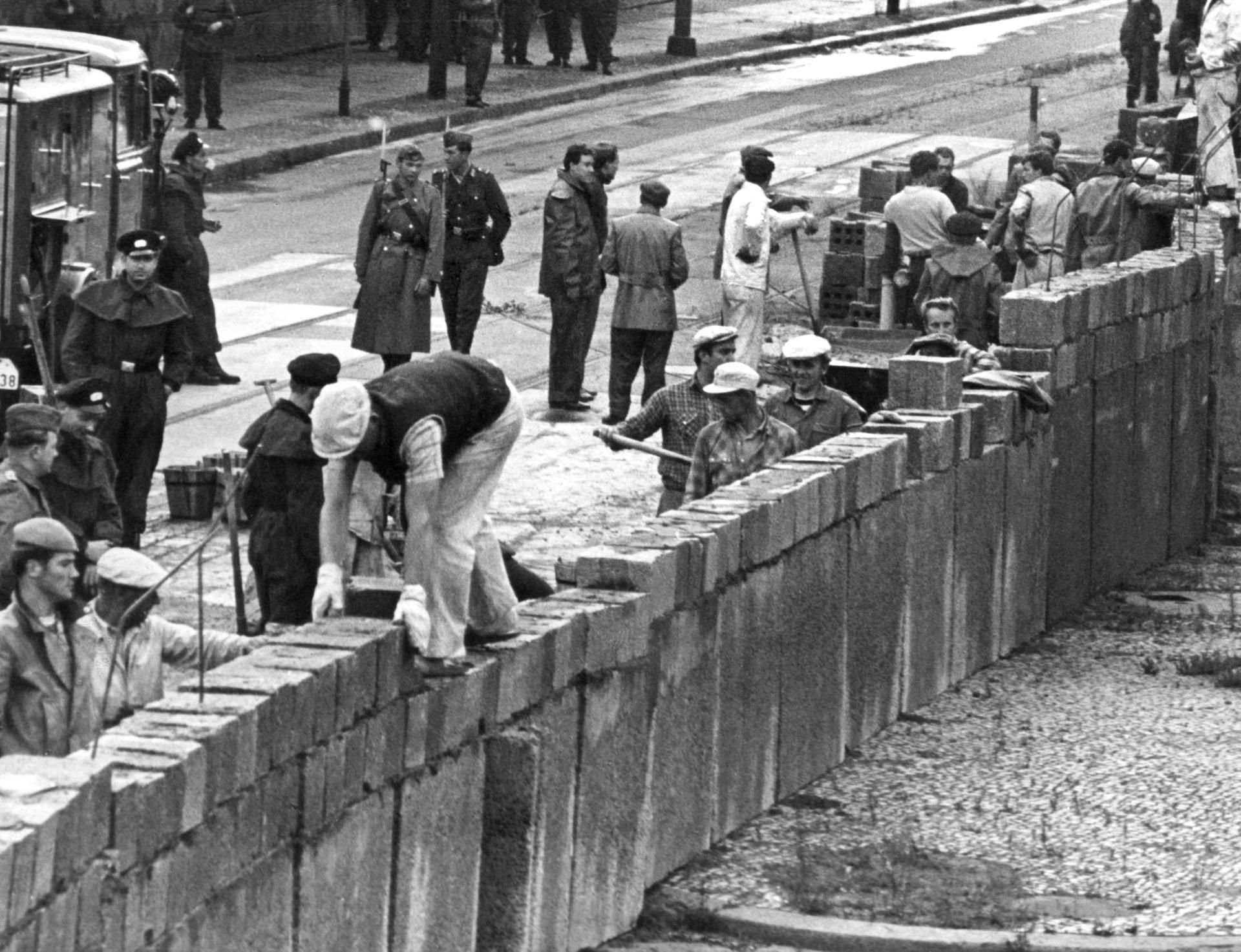 Unter der Aufsicht von bewaffneten Volkspolizisten errichtet eine Ostberliner Maurerkolonne am an der sowjetisch-amerikanischen Sektorengenze am Potsdamer Platz eine Mauer.