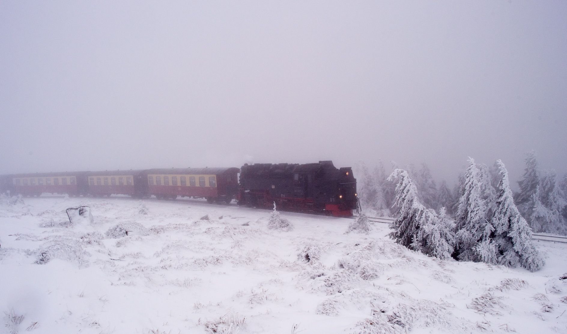 Ein Zug der Brockenbahn der Harzer Schmalspurbahnen (HSB) fährt durch eine verschneite Winterlandschaft zu Tal.