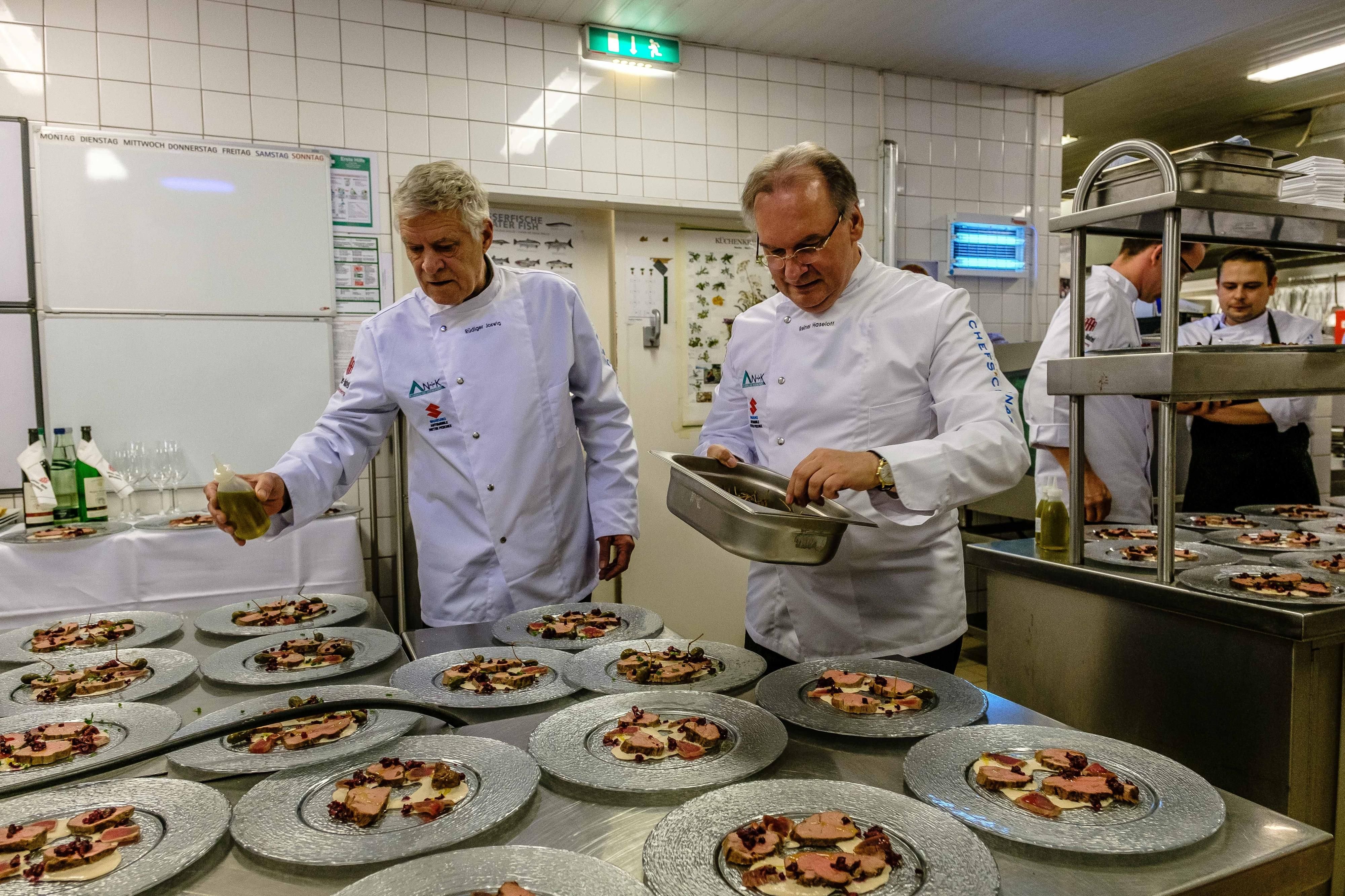 Schauspieler Rüdiger Joswig (u. a. "Küstenwache") steht mit Reiner Haseloff (re.) ebenfalls für den guten Zweck in der Küche des Luther-Hotels in Wittenberg. Der Schauspieler verteilt das Zitronenöl auf den Schweinebäckchen, die als zweiter Gang serviert werden.