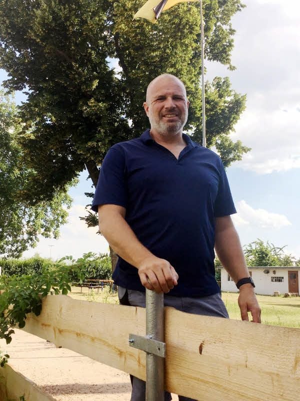 Grundstückseigentümer und „Bergstädter“-Vereinsvorsitzender Stefan Mutz steht vor der imposanten Linde auf dem zentralen Platz an einem neuen Holzzaun, den die Mitglieder montiert haben.