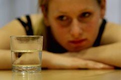 Eine Frau schaut auf ein bis zur Hälfte gefülltes Glas, das auf einem Tisch steht. «Optimismus und Pessimismus sind eine Frage der Perspektive», sagt Tania Konnerth, Autorin des Buches «Zum Glück Optimist». (Foto: ddp)