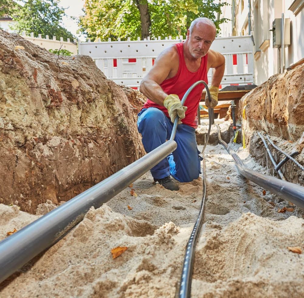 Neben Fernwärmeleitungen werden auch Trink- und Abwasserhausanschlüsse und wie hier von Thilo Mangold Elektrokabel für eine neue LED-Straßenbeleuchtung unter dem Gehweg der Kustrenaer Straße verlegt.