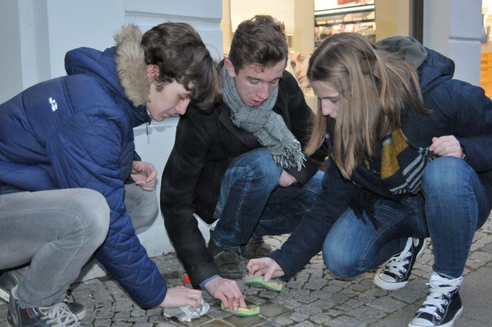 Lukas Villin (v.li.), Till Mohs und Dana Luisa Börnicke putzen die Stolpersteine vor der Parfümerie „Flair“.