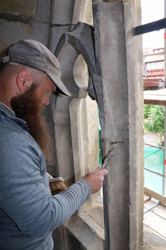 Steinmetz Ralf Herzog von den Werkstätten für Denkmalpflege, bessert Fehlstellen am Maßwerk der Fenster aus.