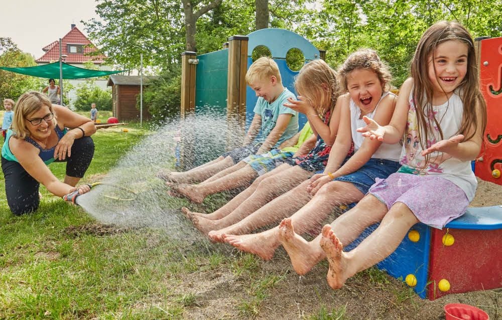 Kirstin Kramersmeyer kühlt die Jungen und Mädchen der Kita Löwenzahn in Bernburg mit einer Fontäne aus dem Wasserschlauch ab.