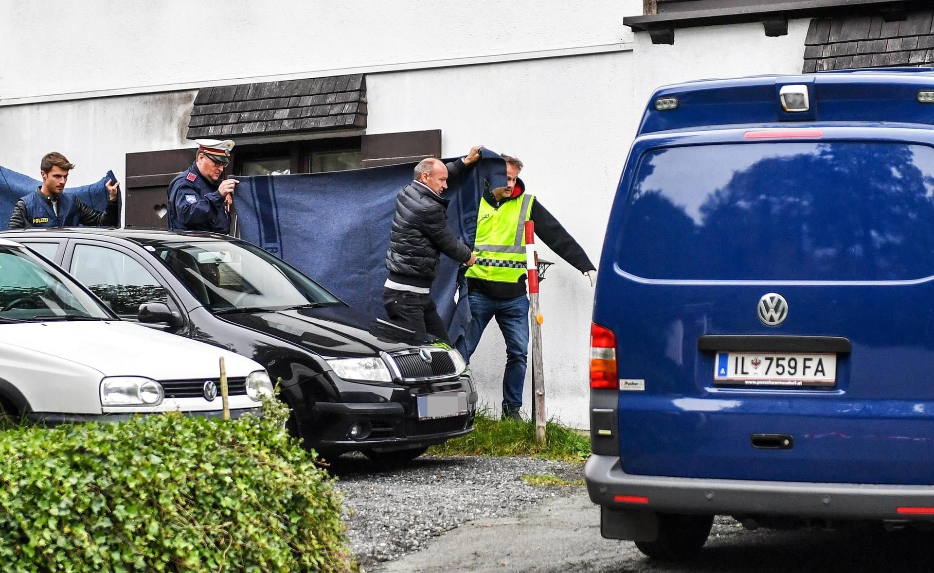 Polizisten schirmen mit Decken den Abtransport der Särge ab.