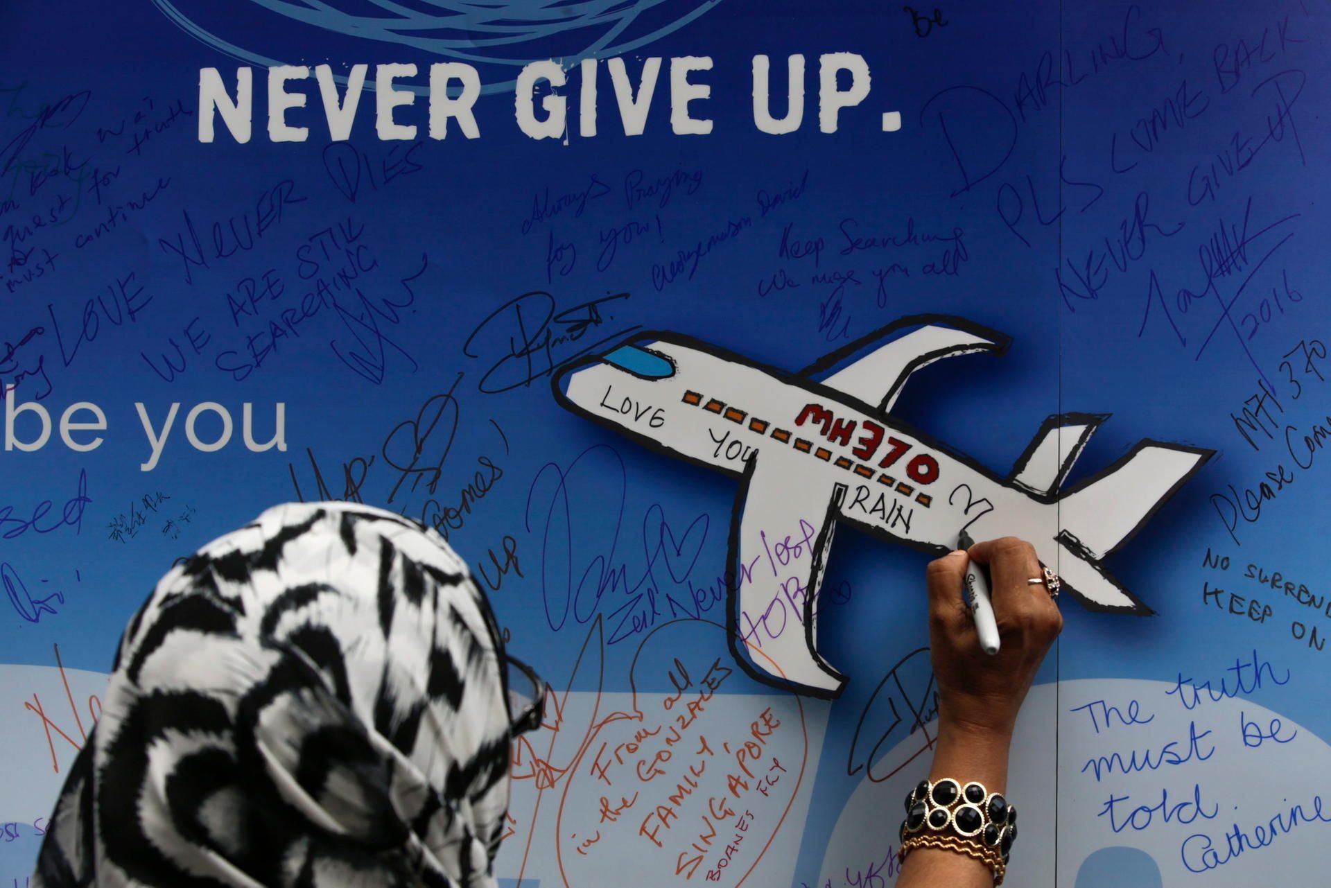 Eine Frau schreibt während einer Gedenkveranstaltung zum Flug MH370 eine Nachricht auf ein Banner.
