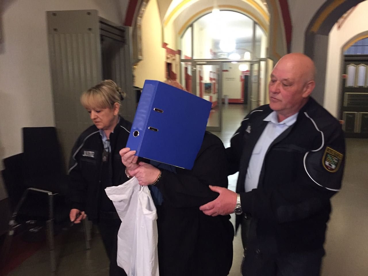 Die Mutter der in Benndorf tot aufgefundenen Babys wird in den Gerichtssaal geführt. Sie verbirgt ihr Gesicht hinter einem Ordner.
