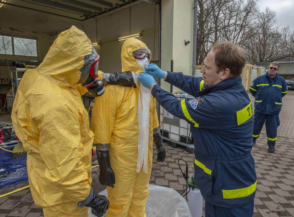 THW-Kollegen helfen, den Schutzanzug auszuziehen, nachdem dieser gründlich desinfiziert wurde.