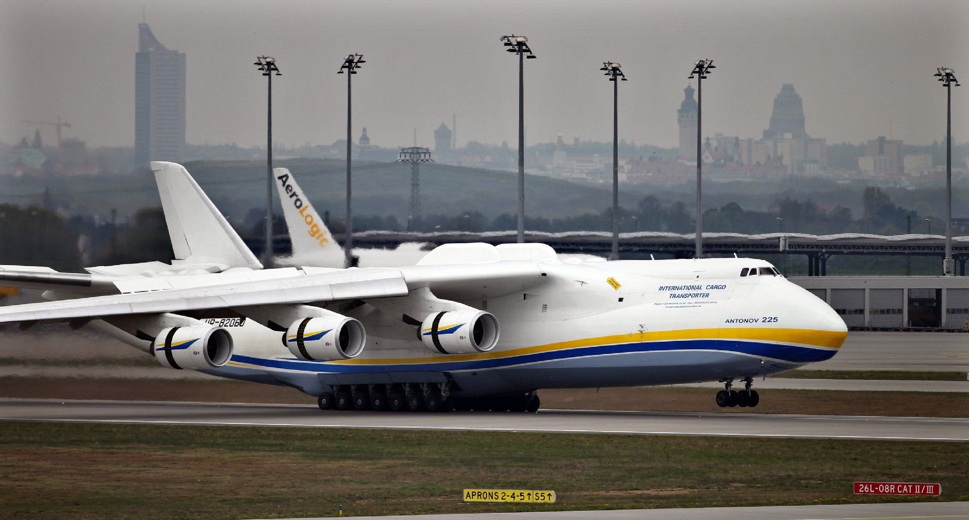 Das größte Frachtflugzeug der Welt, die Antonov AN 225, landet im April 2010 auf dem Flughafen Leipzig/Halle, im Hintergrund die Skyline von Leipzig.
