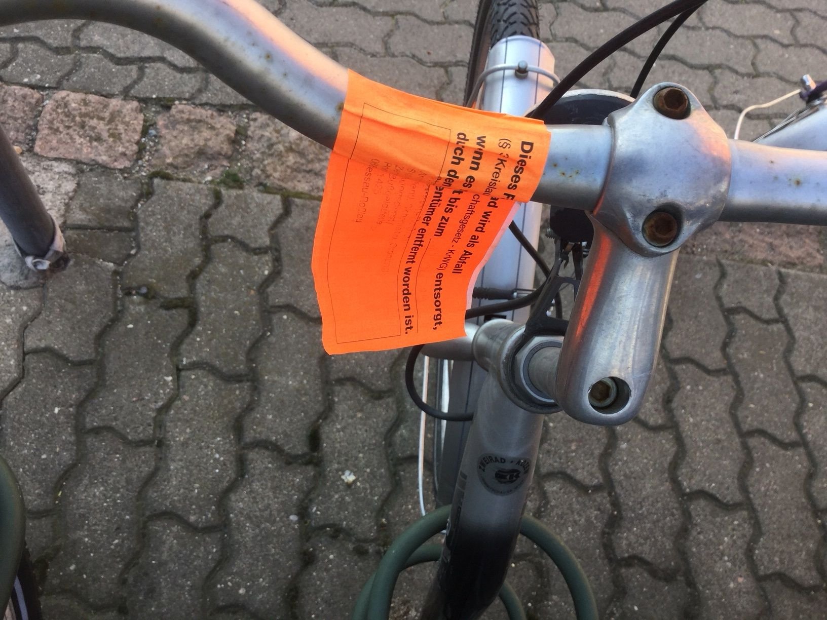Einer der orangefarbenen Sticker klebt am Lenkrad eines Fahrrades.