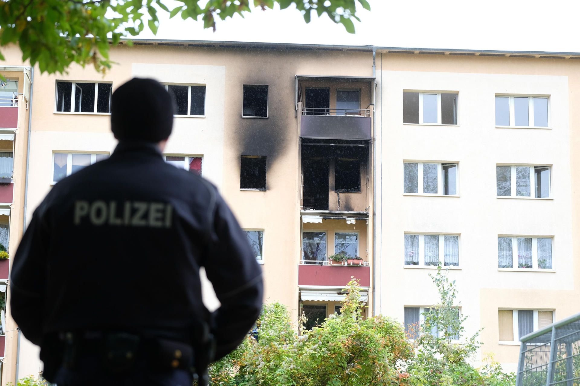 Ein Polizist steht am 7. Oktober 2017 in Leipzig (Sachsen) vor einem Wohnhaus, an dem Spuren eines Brandes zu sehen sind.