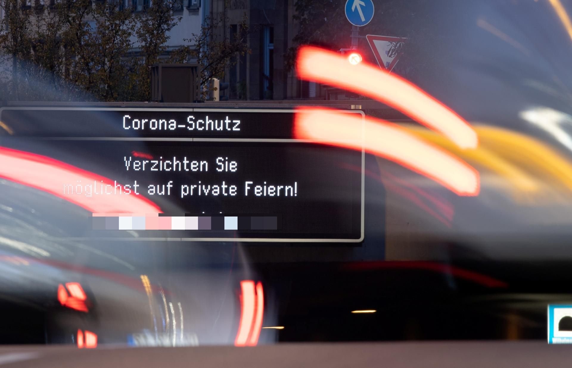 Autos passieren eine elektronische Anzeige, auf der steht: „Corona-Schutz. Verzichten Sie möglichst auf private Feiern!“