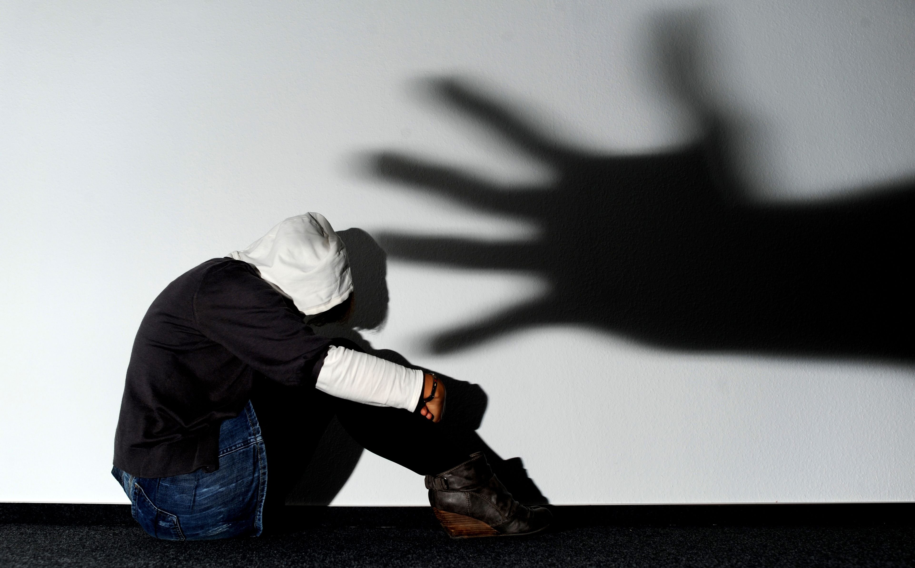 Ein Mädchen sitzt vor einer Wand, auf der der Schatten einer Hand groß zu sehen ist