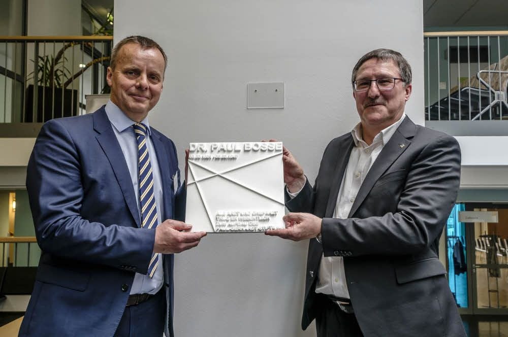 Dr. Henning Rosenberg (li.), Geschäftsführer des Paul-Gerhardt-Stiftes, und Superintendent Christian Beuchel hängen gemeinsam die Gedenkplakette Paul Bosses im Foyer auf.