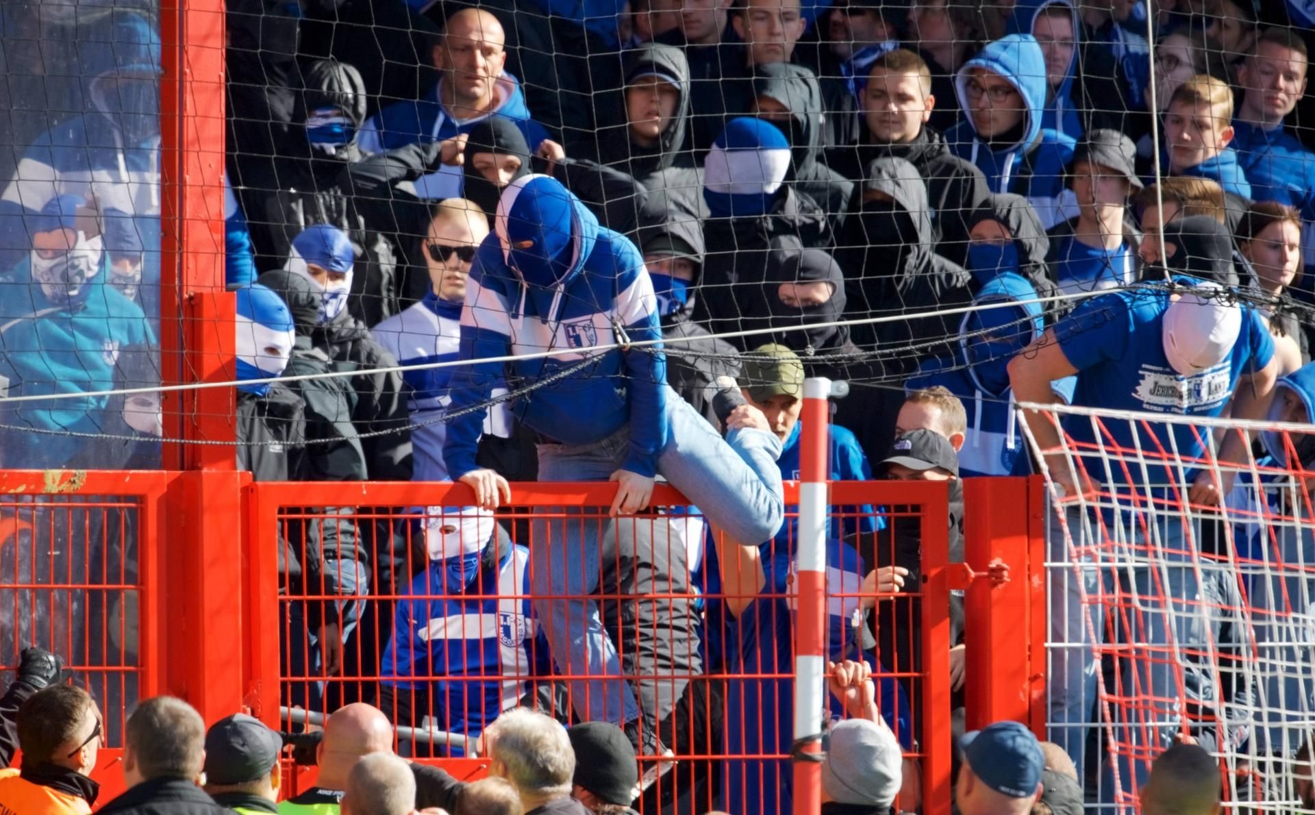 Ein vermummter FCM-Fan will über den Zaun in den Innenraum klettern.