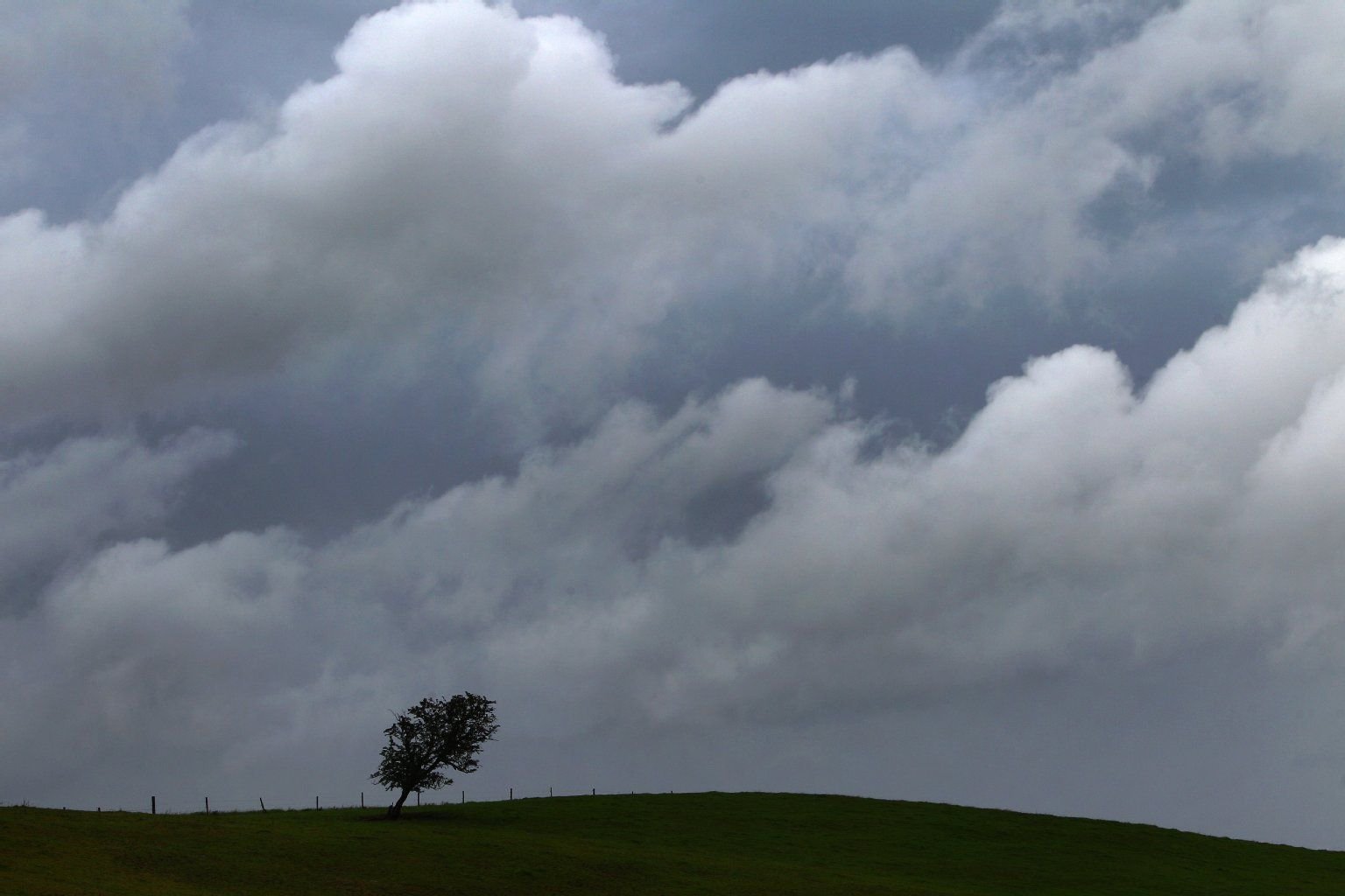 Regenwolken hängen über einem Hügel.