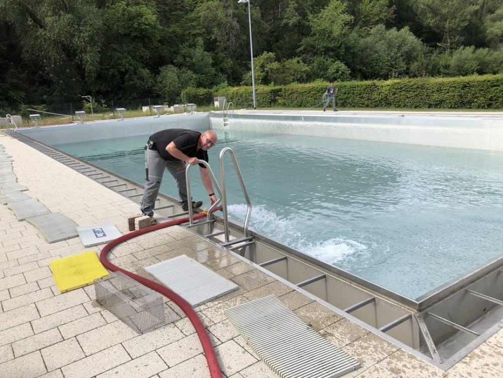 Ein Mitarbeiter des Bauhofs der Stadt Thale hängt einen Schlauch ins Schwimmerbecken des Sommerbads. Bis Dienstag wird es komplett befüllt sein.