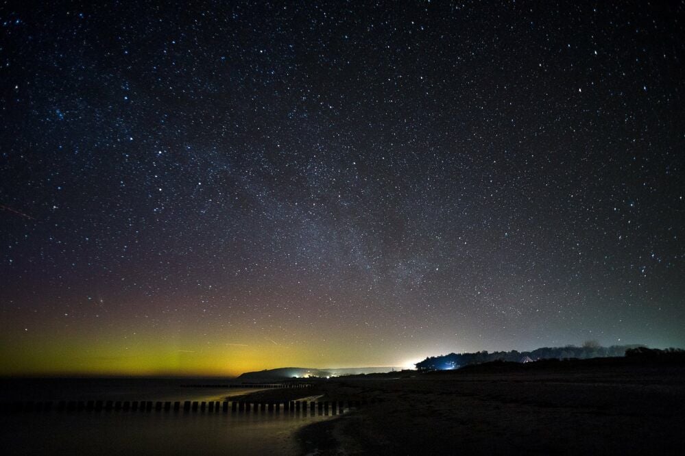 Hiddensee bei Nacht: Neben Tausenden von Sternen ist am Horizont ein gelbgrünes Polarlicht zu sehen.