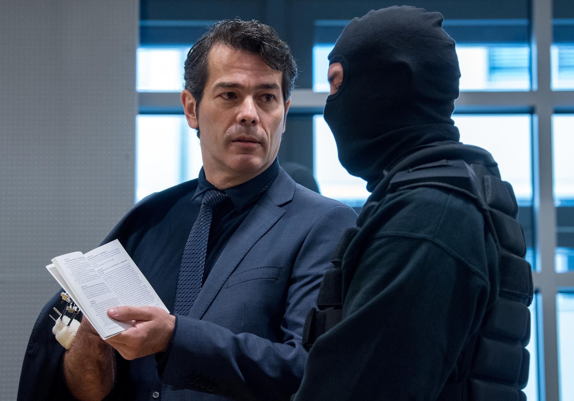 Adrian Ursache (l.) zeigt im Landgericht in Halle vor Prozessbeginn einem Justizbeamten im Gerichtssaal das Grundgesetz.