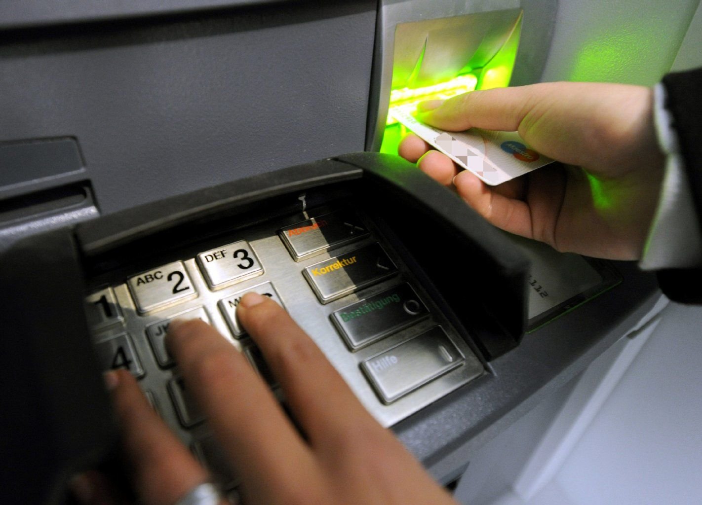 Ein Kunde steht mit einer EC-Karte in an der Tastatur eines Geldautomaten.