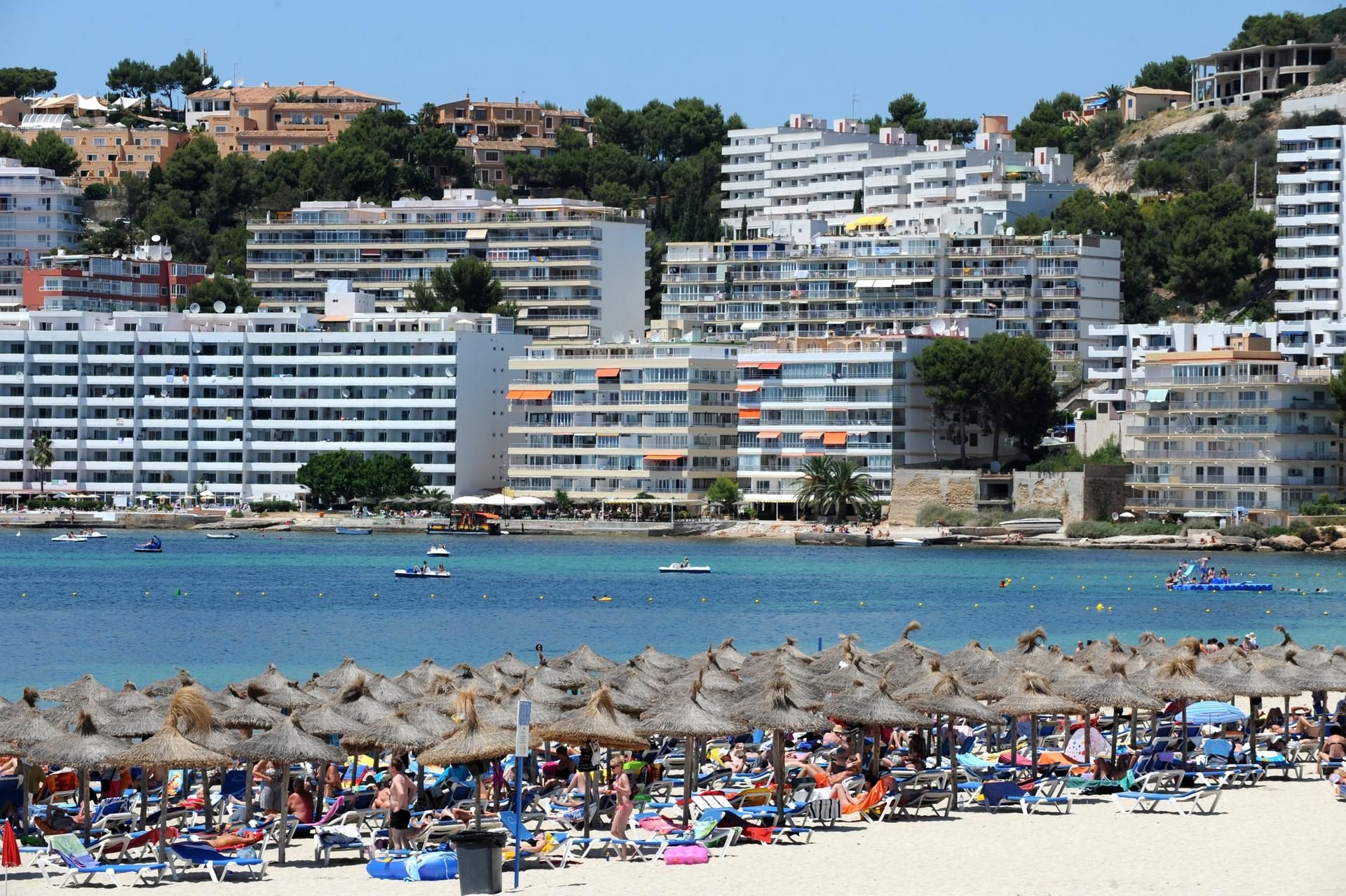 Sonnenschirme und Liegen füllen einen Strand vor zahlreichen Hotelbauten an der Küste Costa de la Calma auf Mallorca (Spanien).