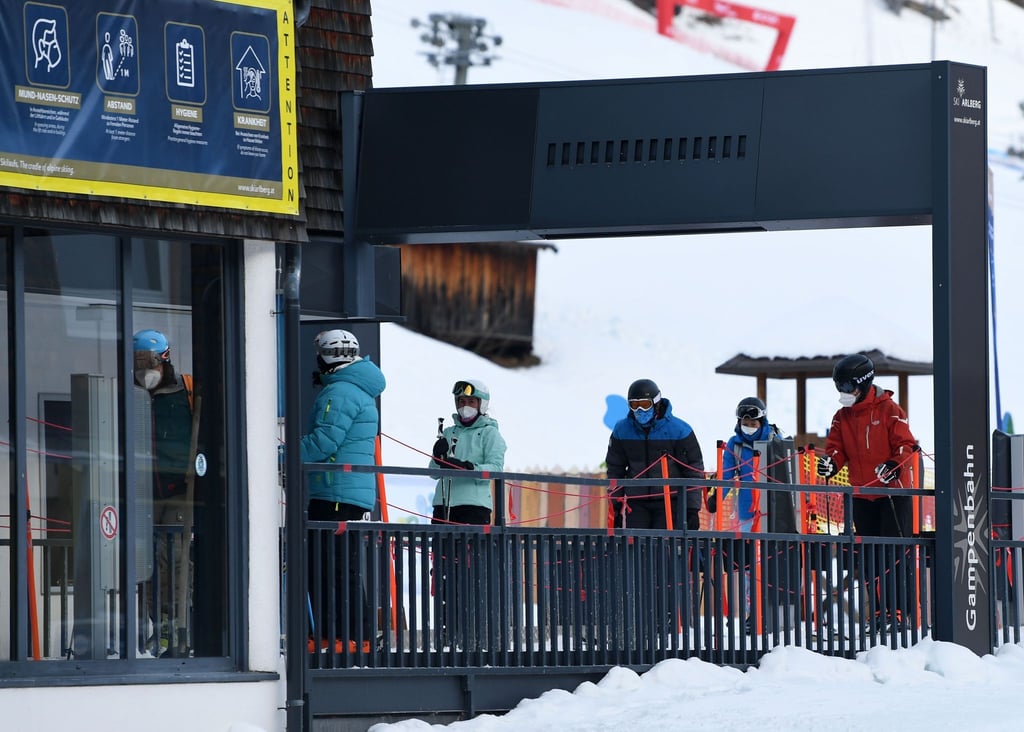 Wintersportler stehen in Tirol mit Mund-Nasen-Schutz an einem Skilift an.