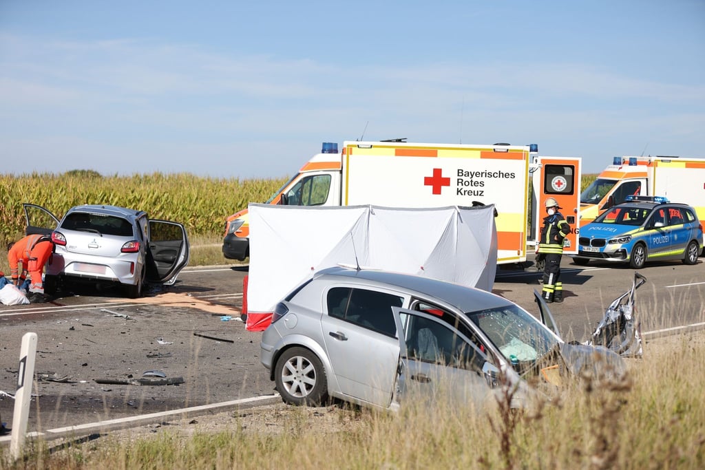 Nach einem Frontalzusammenstoß stehen zwei Autos und mehrere Rettungsfahrzeuge auf einer Bundesstraße.