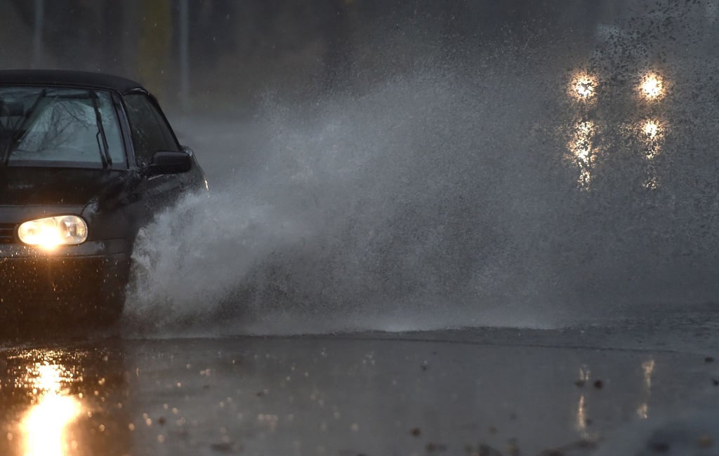 Ein Auto fährt durch eine tiefe Pfütze die sich durch Starkregen auf einer Straße gebildet hat.