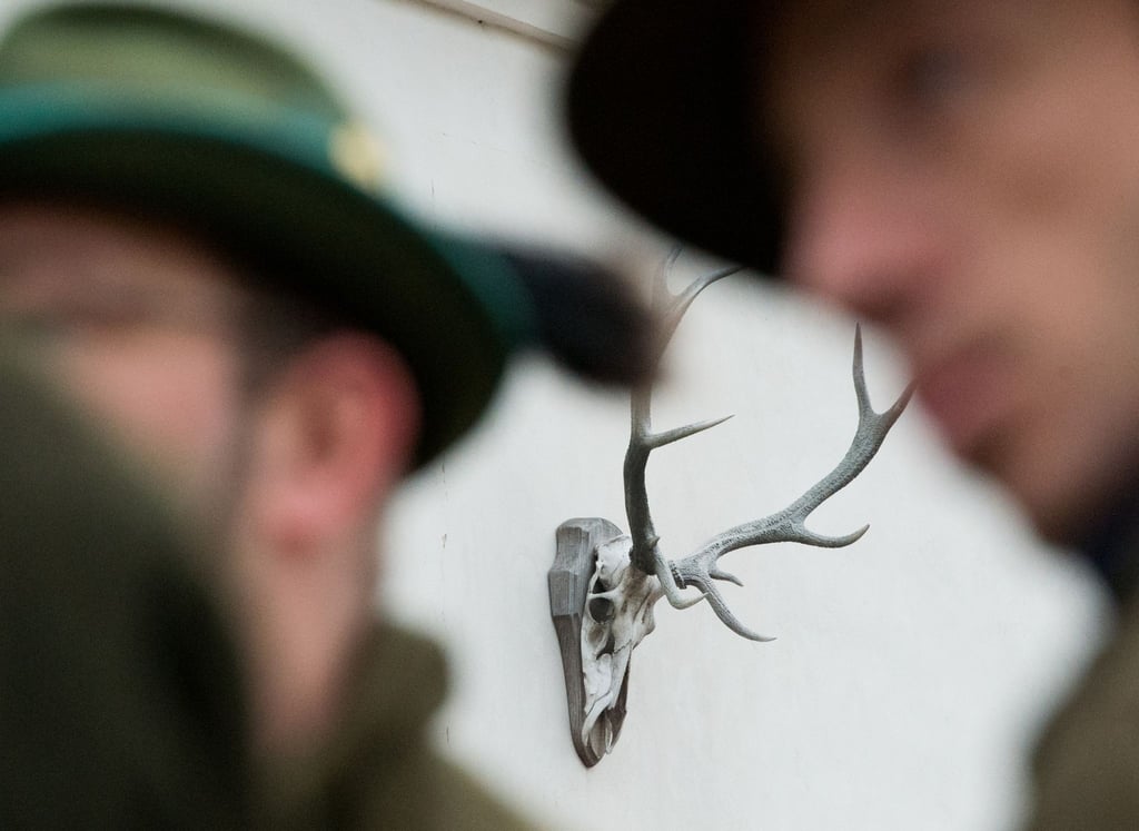 Jäger stehen vor einem Haus, an dem ein Geweih hängt.