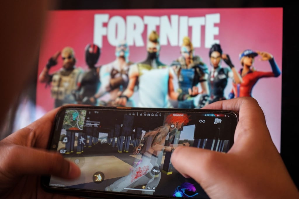 Ein Kind spielt ein Spiel auf einem Mobiltelefon mit einem Bild des Fortnite-Spiels auf dem Computerbildschirm im Hintergrund. (Archivbild)