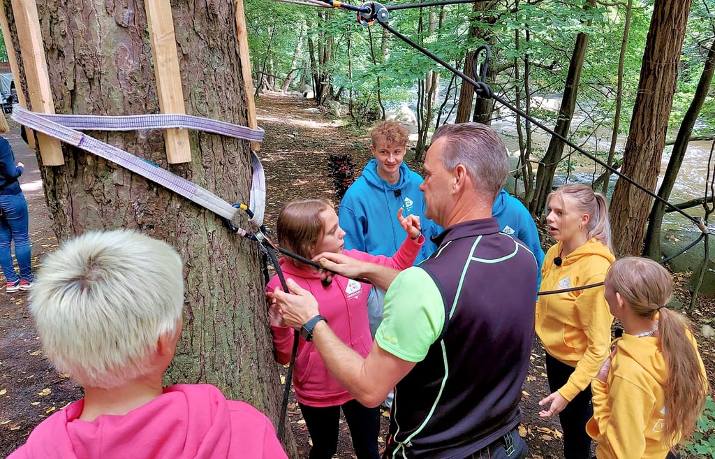 Outdoor-Experte Lars Spanger erklärt den drei Freundespaaren die Funktionen verschiedener Ausrüstungsstücke für die Seilrutsche über die Bode.