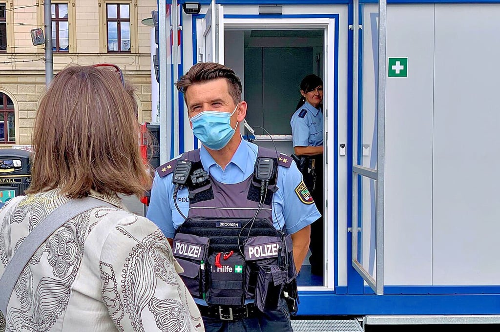 Andreas Dockhorn spricht vor der mobilen Polizeiwache auf dem Markt mit einer Passantin. Bis zum 3. Oktober ist die Polizei hier präsent.