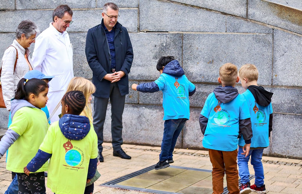 Anne-Katrin Fritzsche, Chefarzt Axel Schobeß und Guido Ulbricht von der Saalesparkasse (v.l.) sehen den Kindern von der Kita Am Weinberg zu, wie sie die Töne des Tanzglockenspiels entdecken.
