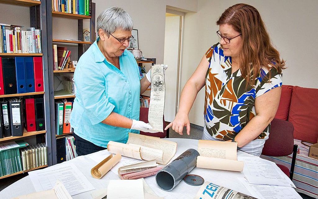 Susanne Kröner (l.) und Pfarrerin Christina Lang nehmen die historischen Dokumente und Münzen in Augenschein, die sich in der Kapsel im Turmknopf der Naumburger Othmarskirche befanden.