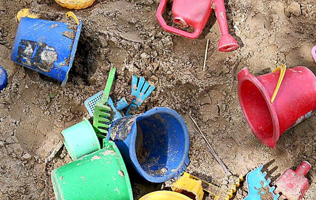Allerhand buntes Spielzeug liegt in einem Sandkasten.