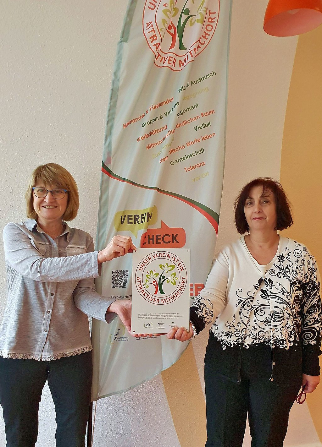 Koordinatorin Martina Schulze und Kollegin Beate Seltmann (v. l.) mit Fahne und Plakette des erfolgreich absolvierten Vereinschecks.