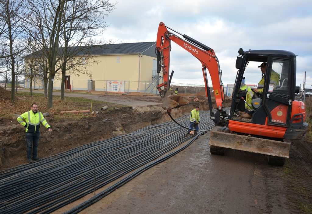 Energienetze-Geschäftsführer Mathias Holzberger zeigt auf die Kabeltrasse, die an die neue Schaltstation (Hintergrund) angeschlossen wird. Ein Mitarbeiter der Firma Omexom aus Genthin zieht ein Schutzrohr.