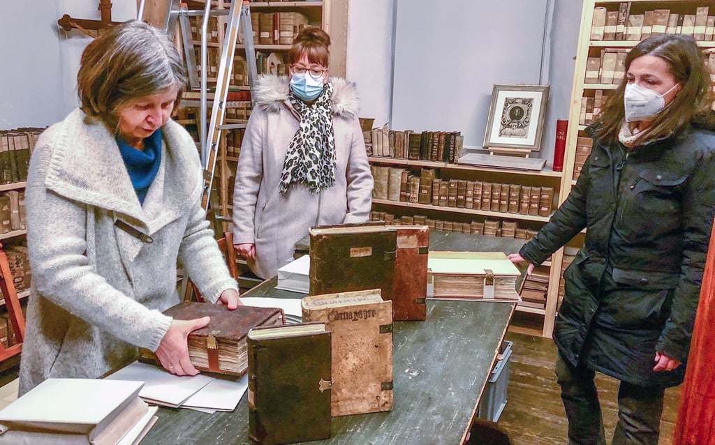 Restauratorin Susanne Lorenz zeigt Ines Enzmann und Carolin Drescher (von links) in der Pfarrbibliothek St. Michael Zeitz die restaurierten Bände.