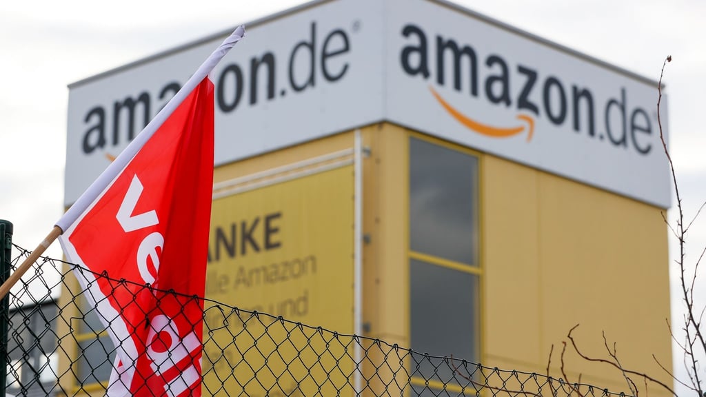 Eine Verdi-Fahne hängt während eines Streiks am Zaun eines Amazon-Versandzentrums. Foto: Jan Woitas/dpa